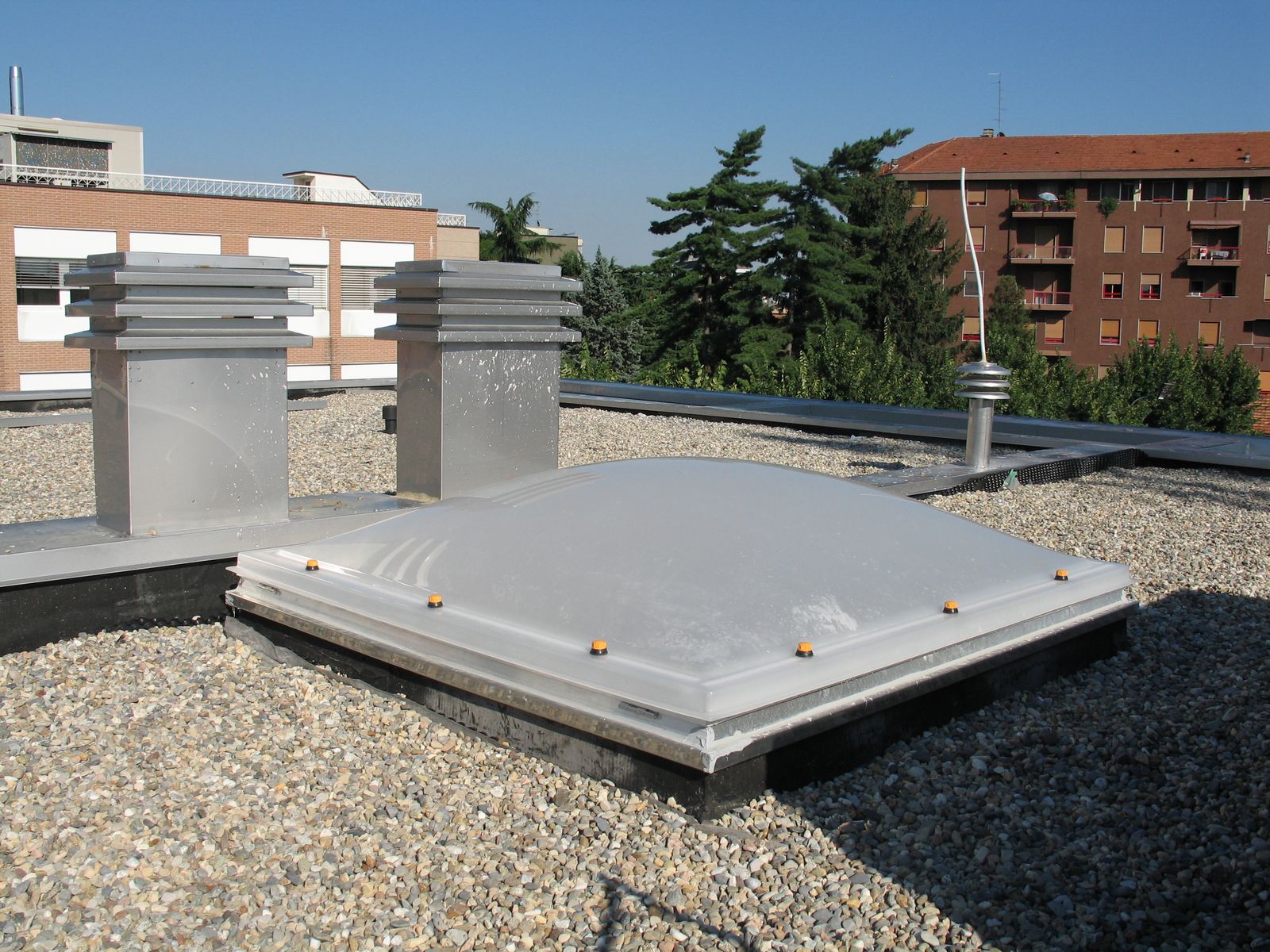 Lucernario termoformato su copertura piana condominiale Lucernario termoformato quadrato su una copertura piana con ghiaia, accanto a torrini di aerazione, in ambiente urbano italiano