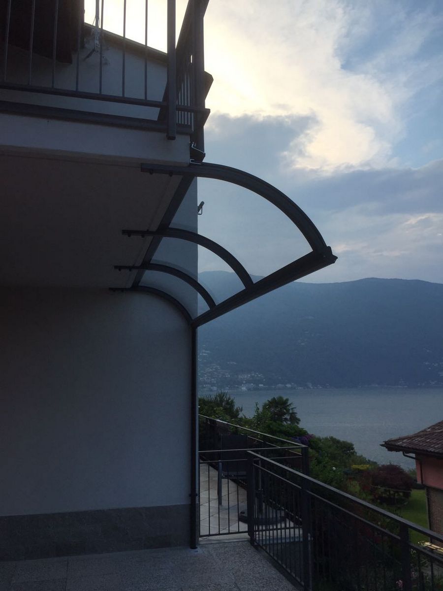 Pensilina sottobalcone ad angolo con vista sul lago Pensilina sottobalcone con profilo curvo ad angolo installata su una terrazza con vista sul lago e le montagne