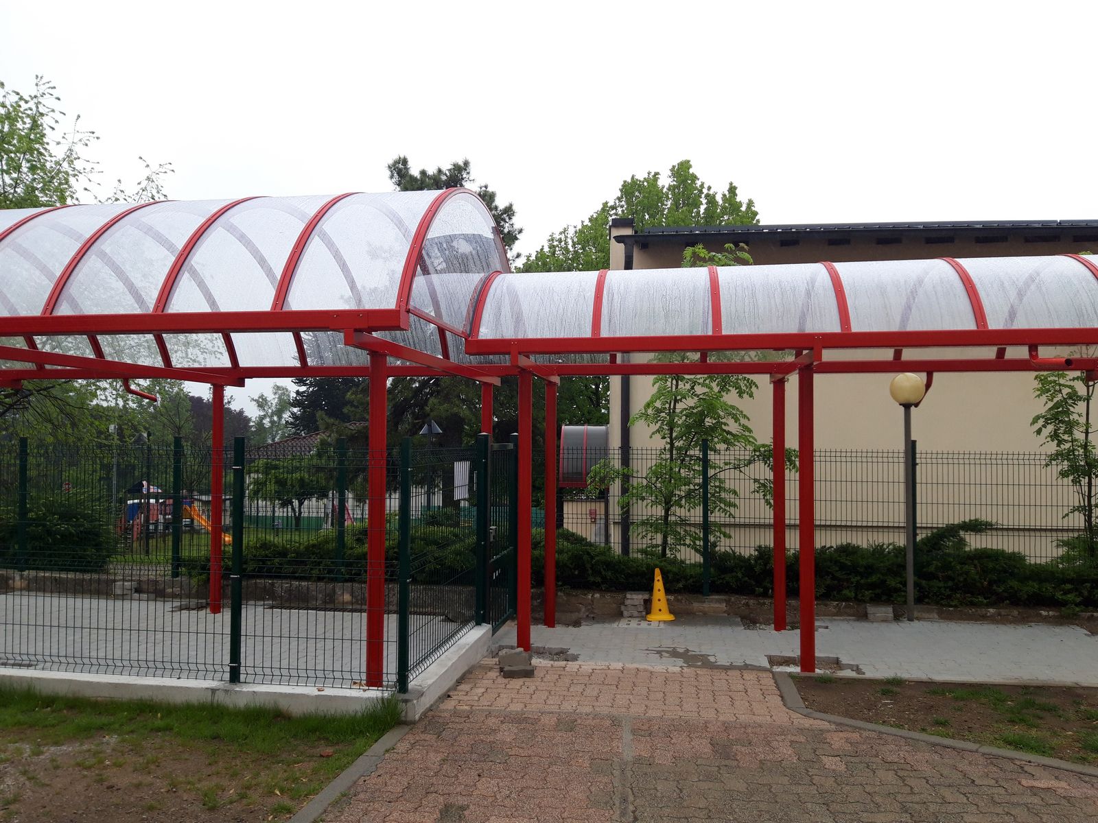 Tunnel ad arco rosso su percorso di scuola Tunnel ad arco in alluminio rosso a copertura di un camminamento vicino a un'area giochi scolastica